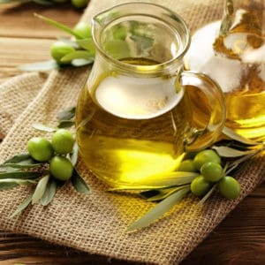 photo of jar of olive oil with green olives and leaves next to it representing manzanillo extra virgin olive oil
