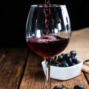 photo of red wine being poured into glass with grapes in background representing organic red wine vinegar