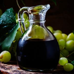 photo of jar of balsamic vinegar with grapes in background representing traditional aged 18 years balsamic vinegar
