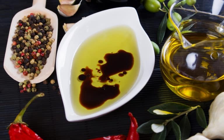 olive oil and vinegar in dish with a chili pepper, garlic, peppercorns, olives and a jar of olive oil