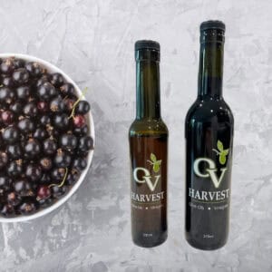 A bowl of black currants and OV harvest balsamic vinegar bottles representing Black Currant Balsamic Vinegar