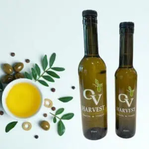 A bowl of olive oil surrounded by olives and leaves and OV Harvest olive oil bottles representing Coratina Extra Virgin Olive Oil