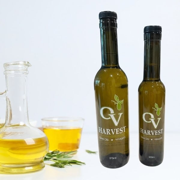 A jar and cup of olive oil and OV Harvest olive oil bottles representing Picual Extra Virgin Olive Oil
