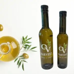 A jar of olive oil with an olive and olive branches and OV Harvest olive oil bottles representing Frantoio Extra Virgin Olive Oil