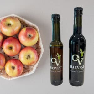 Apples in a white basket and OV Harvest balsamic vinegar bottles representing Gravenstein Apple White Balsamic Vinegar