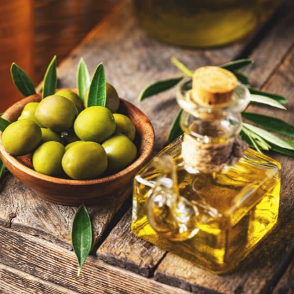 Image of a small bottle of olive oil sitting next to a bowl of green olives representing Barnea Extra Virgin Olive Oil