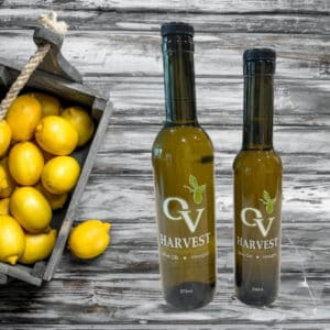 Basket of lemons on a wood background and OV Harvest olive oil bottles representing Lemon Olive Oil