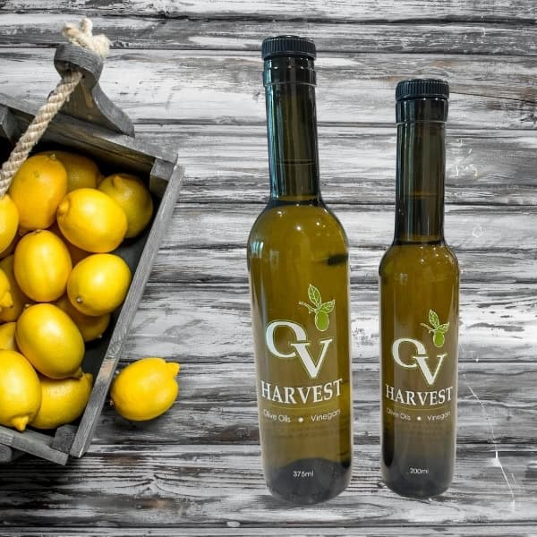 Basket of lemons on a wood background and OV Harvest olive oil bottles representing Lemon Olive Oil