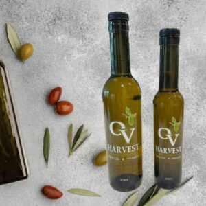 Bottle of olive oil, olives spread around, leaves, and OV Harvest olive oil bottles representing Hojiblanca Extra Virgin Olive Oil