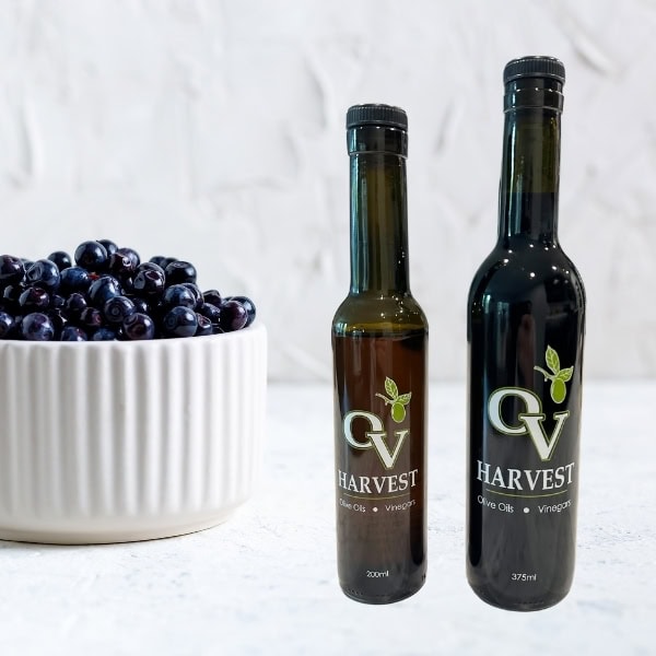 Bowl of blueberries and OV Harvest balsamic vinegar bottles representing Blueberry Balsamic Vinegar