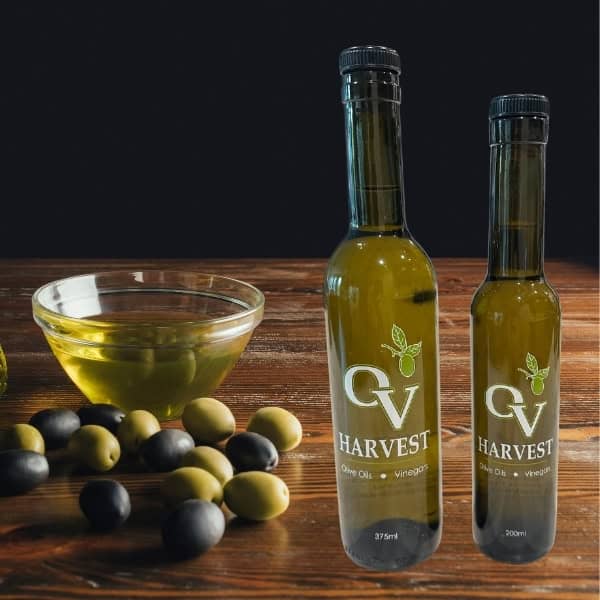 Bowl of olive oil and loose olives and OV Harvest olive oil bottles on a wood table representing Picholine Extra Virgin Olive Oil