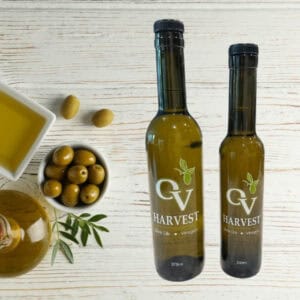 Bowl of olive oil, bowl of olives, jar of olive oil, leaves, and OV Harvest olive oil bottles representing Galega Extra Virgin Olive Oil
