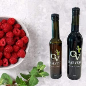 Bowl of raspberries and OV Harvest balsamic vinegar bottles representing Cascadian Wild Raspberry White Balsamic Vinegar