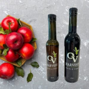 Bowl of red apples sitting on gray stone table and OV Harvest balsamic vinegar bottles representing Red Apple Balsamic Vinegar