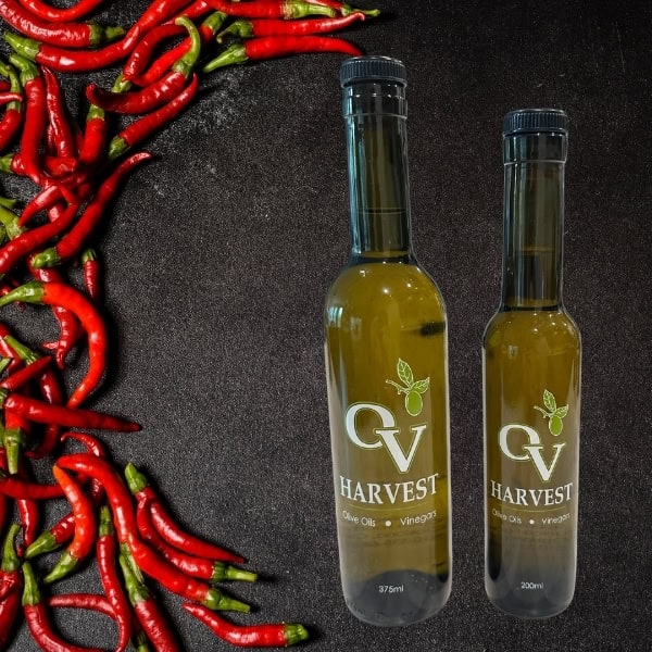 Bright red chili peppers and OV Harvest olive oil bottles representing Red Cayenne Chili Olive Oil