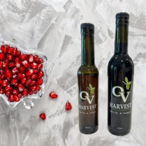 Glass bowl of pomegranate seeds and OV Harvest balsamic vinegar bottles representing Pomegranate Balsamic Vinegar