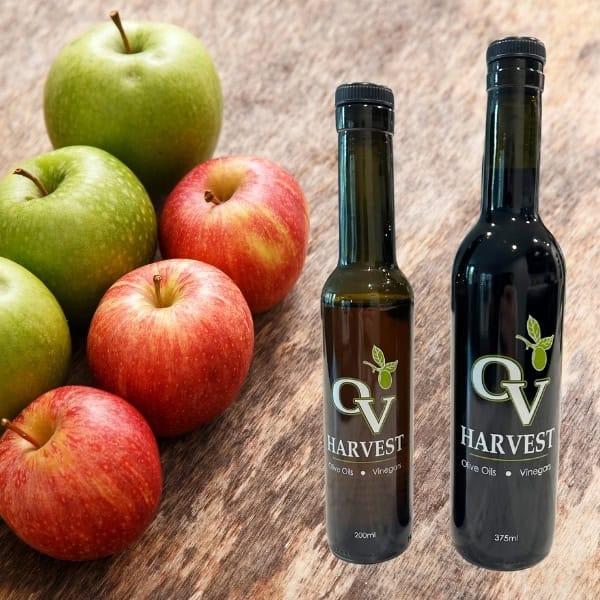 Green and red apples in a row and OV Harvest vinegar bottles representing Raw Unfiltered Organic Apple Cider Vinegar