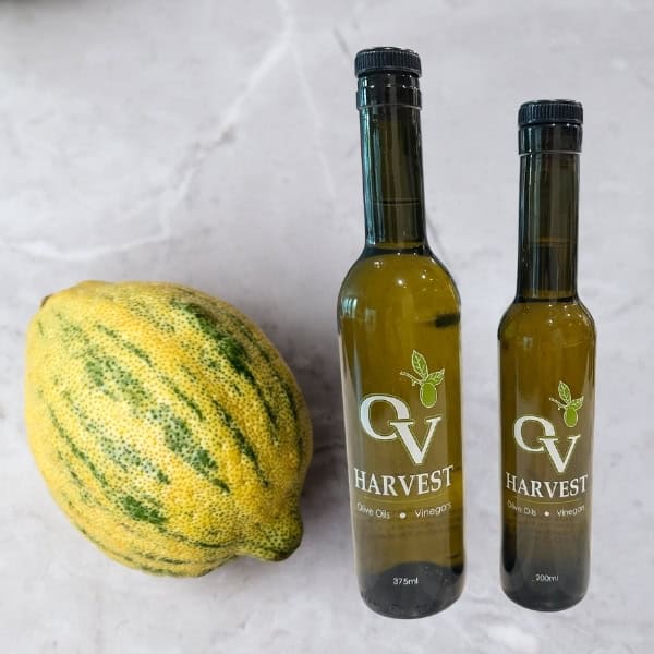 Image of a green lemon next to bottles of OV Harvest Olive Oil representing Green Lemon Olive Oil