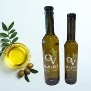 Olive oil in a dish with olives and branches and OV Harvest olive oil bottles representing Cobrançosa Reserve olive oil