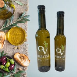 Olive oil jar, slices of bread, olive oil in a dish and OV Harvest olive oil bottles representing Koroneiki Olive Oil