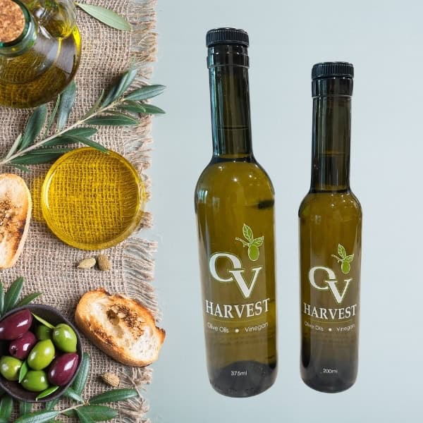 Olive oil jar, slices of bread, olive oil in a dish and OV Harvest olive oil bottles representing Koroneiki Olive Oil