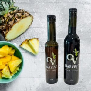 Pieces of pineapple in a bowl, pineapples and OV Harvest balsamic vinegar bottles representing Pineapple White Balsamic Vinegar