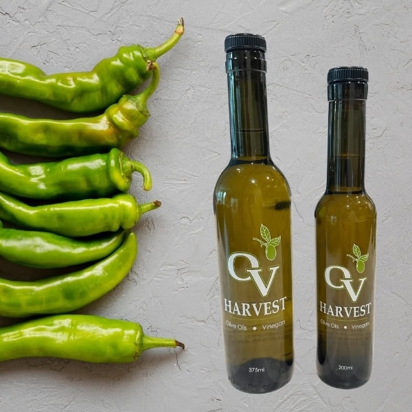 Row of green chilies and OV Harvest olive oil bottles representing Baklouti Green Chili Olive Oil
