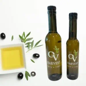Square bowl of olive oil, four olives, olive branches and OV Harvest olive oil bottles representing Koroneiki Extra Virgin Olive Oil