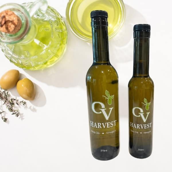 Two olives, a jar of olive oil, a cup of olive oil and OV Harvest olive oil bottles representing Velagosht