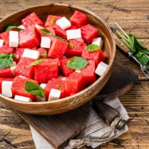 Cubes of watermelon and feta cheese with mint leaves in a wooden bowl.