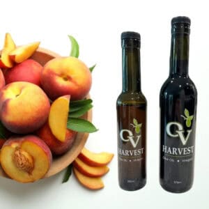 Wooden bowl of peaches and OV Harvest balsamic vinegar bottles representing Peach White Balsamic Vinegar