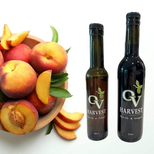 Wooden bowl of peaches and OV Harvest balsamic vinegar bottles representing Peach White Balsamic Vinegar